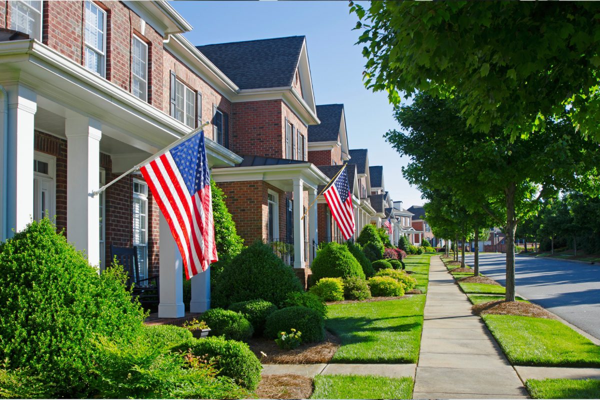 Row of American flags displayed on suburban homes on a sunny day.