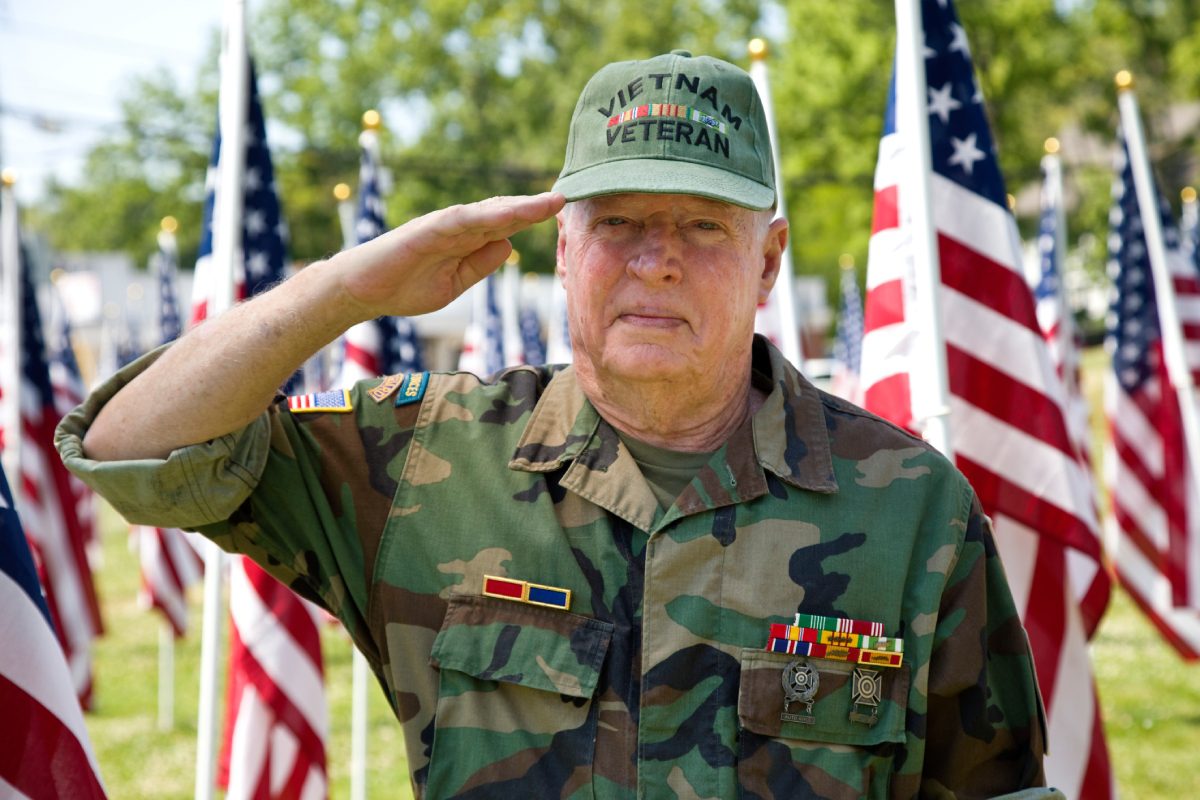 A veteran in military uniform saluting with flags in the background.