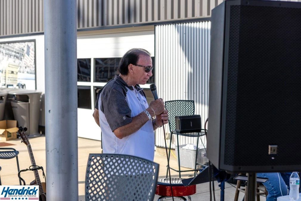 Man speaking into a microphone outdoors near a building.