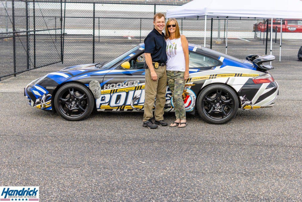 Two people pose beside a Hendrick-branded race car supporting veteran outreach.